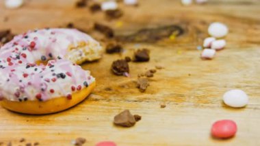 Pembe kremayla süslenmiş pembe çörekler. Çörekler şekerle süslenmiş bir kağıt parçasının üzerinde. Makro ve kaydırma atışı. Şekerler ağır çekimde hareket ediyor. Fırın ve yemek konsepti. Çeşitli renkli çörekler.