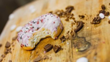 Pembe kremayla süslenmiş pembe çörekler. Çörekler şekerle süslenmiş bir kağıt parçasının üzerinde. Makro ve kaydırma atışı. Şekerler ağır çekimde hareket ediyor. Fırın ve yemek konsepti. Çeşitli renkli çörekler.