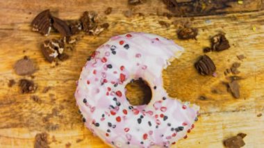 Pembe kremayla süslenmiş pembe çörekler. Çörekler şekerle süslenmiş bir kağıt parçasının üzerinde. Makro ve kaydırma atışı. Şekerler ağır çekimde hareket ediyor. Fırın ve yemek konsepti. Çeşitli renkli çörekler.