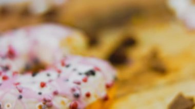 Pembe kremayla süslenmiş pembe çörekler. Çörekler şekerle süslenmiş bir kağıt parçasının üzerinde. Makro ve kaydırma atışı. Şekerler ağır çekimde hareket ediyor. Fırın ve yemek konsepti. Çeşitli renkli çörekler.