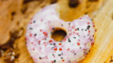 Pembe kremayla süslenmiş pembe çörekler. Çörekler şekerle süslenmiş bir kağıt parçasının üzerinde. Makro ve kaydırma atışı. Şekerler ağır çekimde hareket ediyor. Fırın ve yemek konsepti. Çeşitli renkli çörekler.