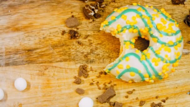 黄色的甜甜圈装饰着蓝色的糖霜 甜甜圈在用糖果装饰的一张纸上 宏观和滑翔机射击 宏观和滑翔机射击 糖果是慢动作的 面包店和食品 — 图库视频影像