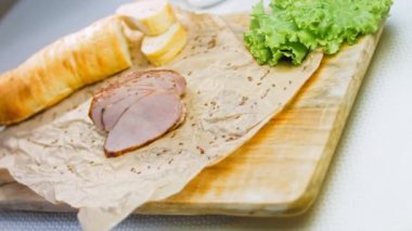 Fransız ekmeğiyle dilimlenmiş domuz filetosu. Sosis retro-stil yemek tepsisinde ve yemek kağıdında. Yavaş çekim kaydırağın üzerinde. Taze marul yaprakları da kullanıyoruz..