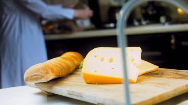 Retro-stil yemek tepsisinde delikleri olan peynir. Kaypak peynir sunum sürecini kaydetti. Arka planda kadın yemekleri hazırlar. Yavaş çekim.