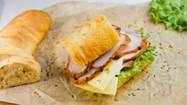 Fransız ekmeği, peynir, marul ve sosisli sandviç. Kaydırma atışı. Arka planda eski bir fırın tepsisi ve yemek kağıdı var..