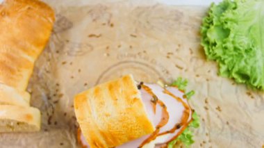 Fransız ekmeği, peynir, marul ve sosisli sandviç. Kaydırma atışı. Arka planda eski bir fırın tepsisi ve yemek kağıdı var..