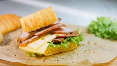 Fransız ekmeği, peynir, marul ve sosisli sandviç. Kaydırma atışı. Arka planda eski bir fırın tepsisi ve yemek kağıdı var..