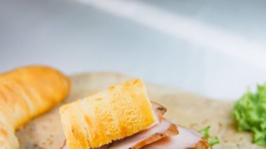 Fransız ekmeği, peynir, marul ve sosisli sandviç. Kaydırma atışı. Arka planda eski bir fırın tepsisi ve yemek kağıdı var..