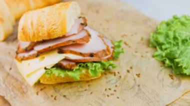 Fransız ekmeği, peynir, marul ve sosisli sandviç. Kaydırma atışı. Arka planda eski bir fırın tepsisi ve yemek kağıdı var..