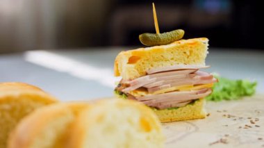 Fransız ekmeği, peynir, marul ve sosisli sandviç. Kaydırma atışı. Arka planda retro fırın tepsisi ve yemek kağıdı var. Üzerine küçük bir salatalık konmuş..