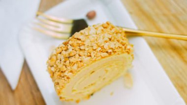 Altın çatallı bir tabakta fıstıklı kek. Arka planda retro-stil yemek tepsisi üzerinde soyulmuş fıstık var. Makro ve sürgülü atış.