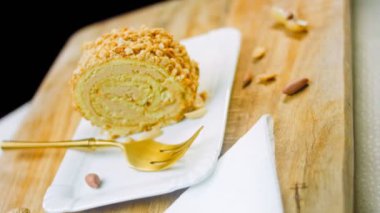 Altın çatallı bir tabakta fıstıklı kek. Arka planda retro-stil yemek tepsisi üzerinde soyulmuş fıstık var. Makro ve sürgülü atış.