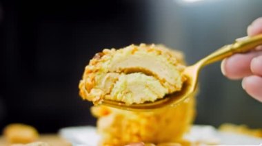 Kadın, altın çatallı fıstıkla sarılmış bir parça kek alıyor. Arka planda retro-stil yemek tepsisi üzerinde soyulmuş fıstık var. Makro ve sürgülü atış.