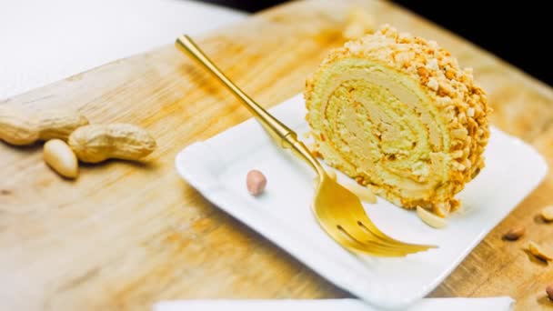 金のフォークで皿の上にピーナッツロールケーキ 背景にはレトロスタイルの料理トレイにピーナツを皮をむいています マクロ撮影とスライダー撮影 — ストック動画