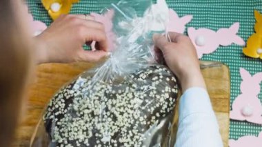 Kadın çikolatalı panettone açıyor. Arka planda kağıttan yapılmış Paskalya tavşanları var. Makro ve sürgülü atış.