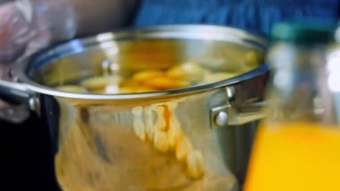 Kadın yeni patatesleri suyla kaynatmak için tencereye koyar. Kaydırıcı ve makro atış.