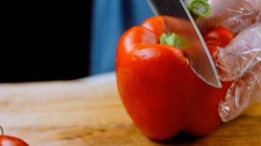 Front view of the young chef cut thin slices of a piece of red pepper with a knife on the cutting board. Front view of a young chef cutting thin slices of a piece of red pepper. Vegetables up close.