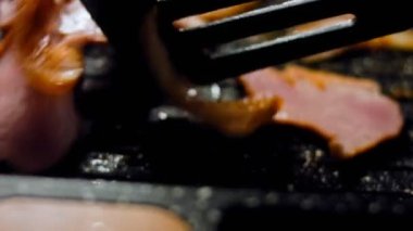 Aşçı kızarmış pastırmayı kaşıkla karıştırır. Kamera ızgarada pastırma pişirmeyi takip ediyor..