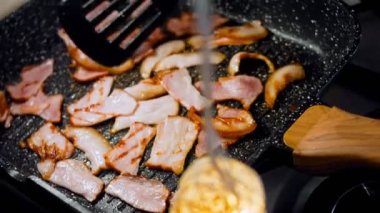 Aşçı kızarmış pastırmayı kaşıkla karıştırır. Kamera ızgarada pastırma pişirmeyi takip ediyor..