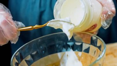 Şef kaşıkla mayonezi şeffaf bir kaseye koyar..