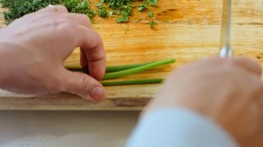 Bir kadının eli, tahta kesme tahtasına saplanmış bir bıçakla yeşil soğan kesiyor. Salata için sebze dilimliyorum.