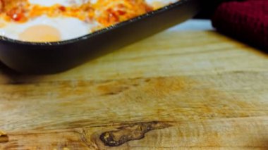 Kadın tavayı chirbuli ile masaya koyuyor. Gürcistan mutfağında kızarmış yumurta, chirbuli. Tavada domatesli yumurta..