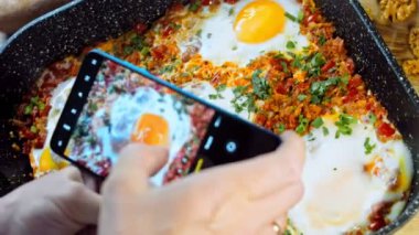 Telefonunuzla yemek fotoğrafları çekiyorsunuz. Gürcistan mutfağında kızarmış yumurta, chirbuli. Tavada domatesli yumurta..