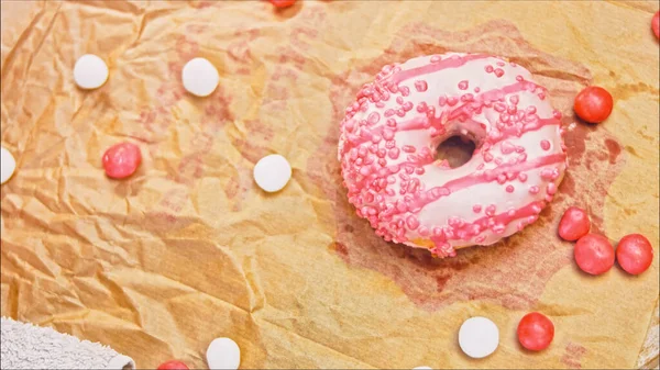 Pink donuts decorated with pink icing. Donuts are on a piece of paper decorated with candy. Macro and slider shooting. The candies move in slow motion. Bakery and food concept.