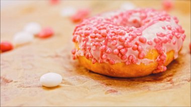 Pembe kremayla süslenmiş pembe çörekler. Çörekler şekerle süslenmiş bir kağıt parçasının üzerinde. Makro ve kaydırma atışı. Şekerler ağır çekimde hareket ediyor. Fırın ve gıda konsepti.