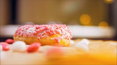 Pembe kremayla süslenmiş pembe çörekler. Çörekler şekerle süslenmiş bir kağıt parçasının üzerinde. Makro ve kaydırma atışı. Şekerler ağır çekimde hareket ediyor. Fırın ve gıda konsepti.