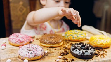 Kız hediyeler arasından seçiyor, parmağını işaret ediyor. Çikolata, marşmelov ve retro pişirme tepsisindeki şekerli çörekler. Donutlar doğal çikolatayla süslenmiş bir kağıdın üzerinde. Makro ve kaydırıcı
