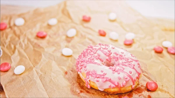 Pink donuts decorated with pink icing. Donuts are on a piece of paper decorated with candy. Macro and slider shooting. The candies move in slow motion. Bakery and food concept.