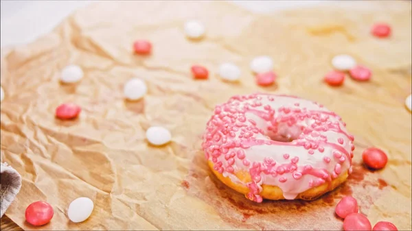 Pink donuts decorated with pink icing. Donuts are on a piece of paper decorated with candy. Macro and slider shooting. The candies move in slow motion. Bakery and food concept.