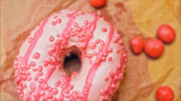 Pink donuts decorated with pink icing. Donuts are on a piece of paper decorated with candy. Macro and slider shooting. The candies move in slow motion. Bakery and food concept.