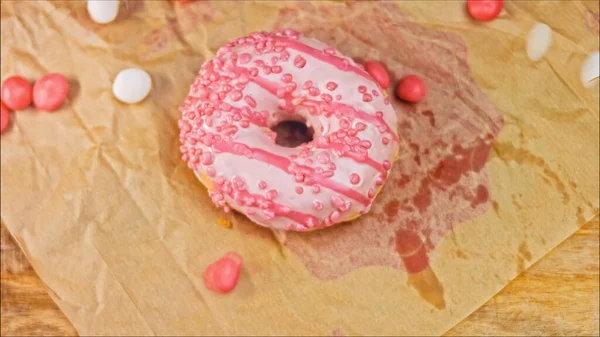 Pink donuts decorated with pink icing. Donuts are on a piece of paper decorated with candy. Macro and slider shooting. The candies move in slow motion. Bakery and food concept.