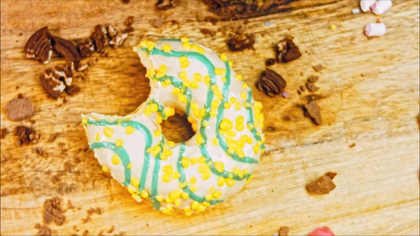 Donut has a mouth-shaped bite. Yellow donuts decorated with blue icing. Donuts are on a piece of paper decorated with candy. Macro and slider shooting. Macro and slider shooting. The candies move in