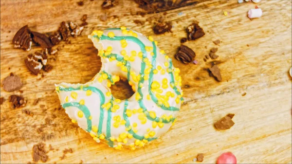 Donut has a mouth-shaped bite. Yellow donuts decorated with blue icing. Donuts are on a piece of paper decorated with candy. Macro and slider shooting. Macro and slider shooting. The candies move in