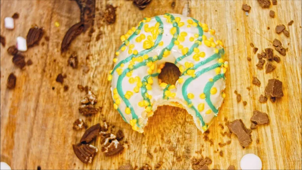 Donut has a mouth-shaped bite. Yellow donuts decorated with blue icing. Donuts are on a piece of paper decorated with candy. Macro and slider shooting. Macro and slider shooting. The candies move in