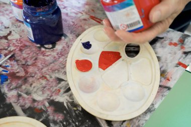 Sanat eserleriyle çizim sınıfı. 4-8 yaş arası çocukların olduğu bir sınıf. Bir kız yeşil bir kağıda parlak renkli bir resim çiziyor.