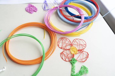 Plastik telden yapılmış oyuncaklar. Masanın üzerinde çok renkli bobinler var. Çocuk pembe 3 boyutlu kalemle rakamlar yapıyor..