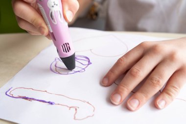 Plastik telden yapılmış oyuncaklar. Masanın üzerinde çok renkli bobinler var. Çocuk pembe 3 boyutlu kalemle rakamlar yapıyor..