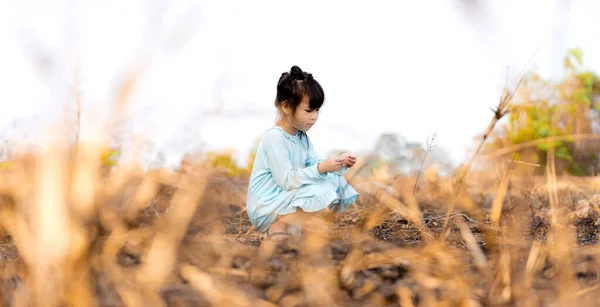 燃える草の後ろの森の中の草の上に座っているかわいい女の子 — ストック写真