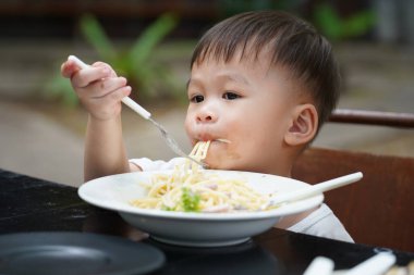 Küçük çocuk lezzetli spagetti yiyor, yeni yürümeye başlayanlar için öğrenme konsepti