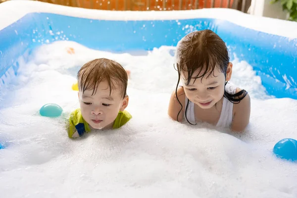 Kız ve erkek kardeş evdeki yüzme havuzunda baloncuklarla oynarken eğleniyorlar. Yaz su oyunu, aile mutluluğu, çocukların mutluluğu.