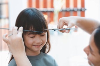 Ön saçlarını kesmek için kadın eli ya da evdeki tatlı Asyalı bir kıza kakül. Anneler çocuklarının saçlarını kesmekten mutlu olurlar. Saç bakımı konsepti