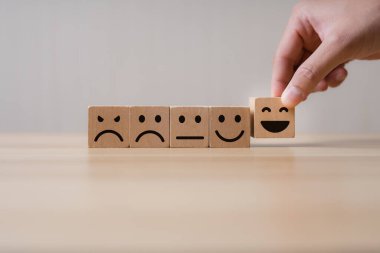 İyi ve etkileyici müşteri hizmetleri kavramı. İş adamının eli ahşap bir blokta gülen bir yüz seçiyor, mükemmel bir iş derecelendirme deneyimi. Müşterilerin yorumları, memnuniyet derecesi