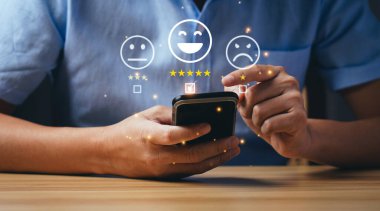 Müşteri ve Tüketici Memnuniyeti Konsepti. İş adamları ya da müşteriler memnuniyetlerini akıllı telefondan ifade ederek 5 yıldız puanı ve gülen surat emojisini seçiyorlar.