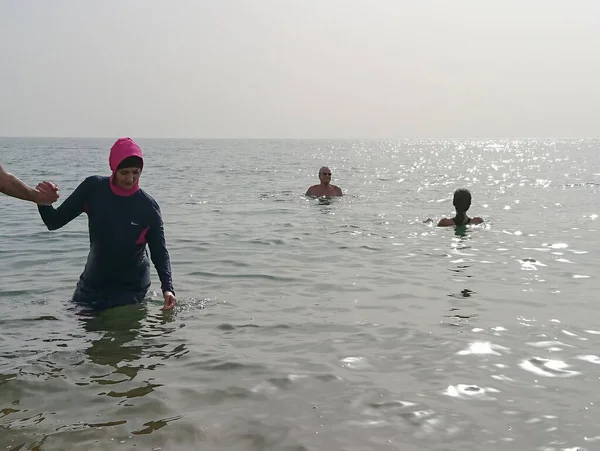 イスラム教徒の女性は完全に死海の塩辛い海でヒジャーブの入浴で覆われて ヨルダン ストック画像