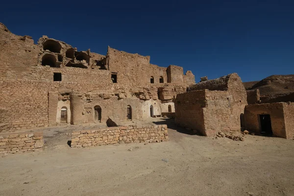 Douiret manzarası, Tunus 'un güneyindeki Tataouine bölgesindeki Berber köyünü modern bir köyün yakınındaki bir tepenin üzerine yıktı. Arkaplanda açık mavi gökyüzü.
