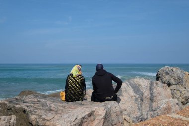 Muslim couple sitting on the rock in front of River Bou Regreg and Kasbah of Udayas fortress in Medina of Rabat, the capital of Morocco. Located on the Atlantic Ocean at the mouth of the river Bou Regreg.